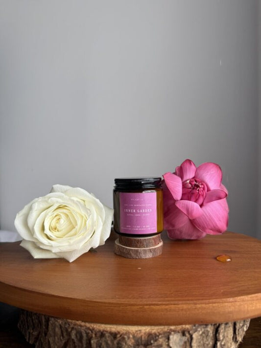 Candle with a pink label on a wooden surface surrounded by flowers