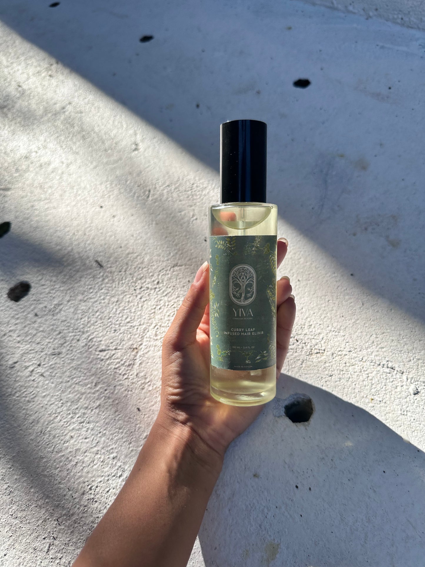 Hand holding a bottle of hair oil against a light-colored surface