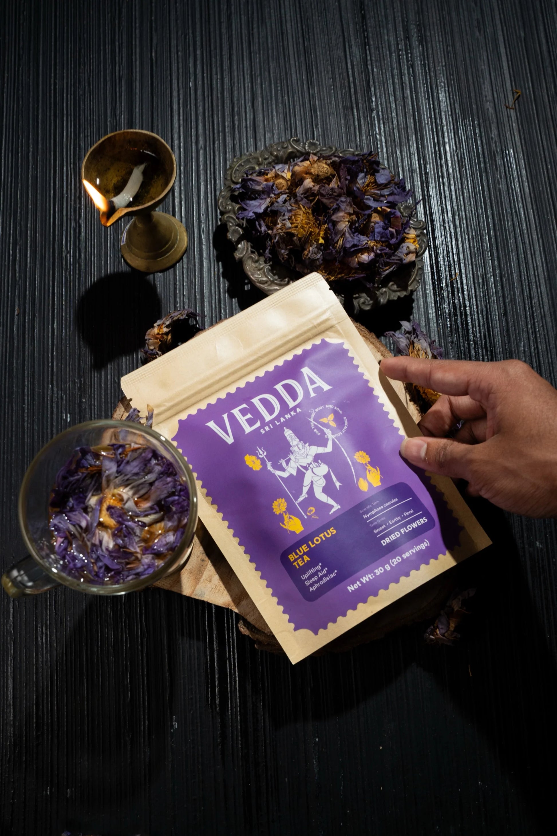 Vedda tea packaging with dried herbs on a dark surface